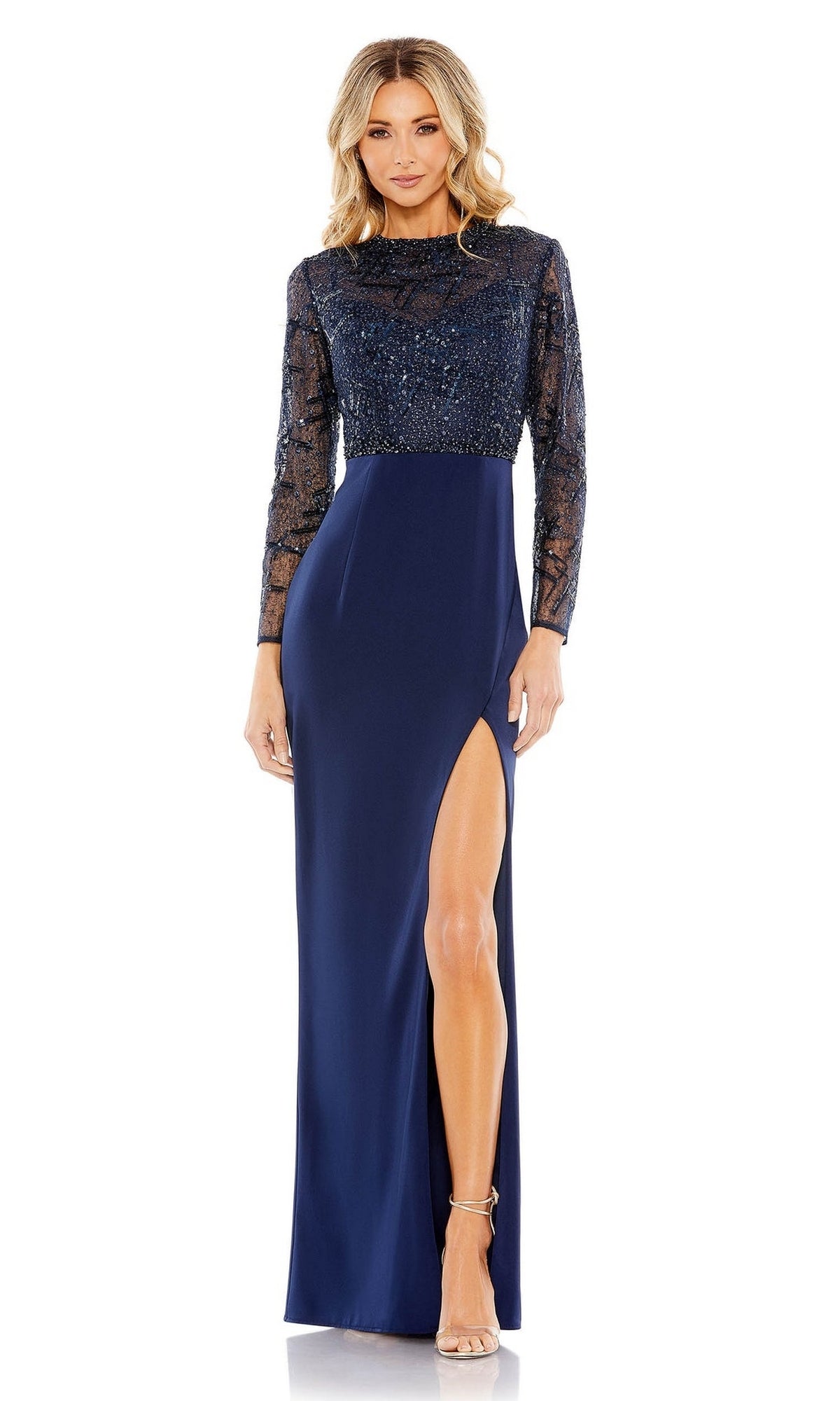 A woman stands facing forward in the Long Sleeve Blue Formal Dress: Mac Duggal 20340, featuring sheer embellished sleeves, a beaded bodice, and a high left leg slit—a stunning choice for formal occasions.